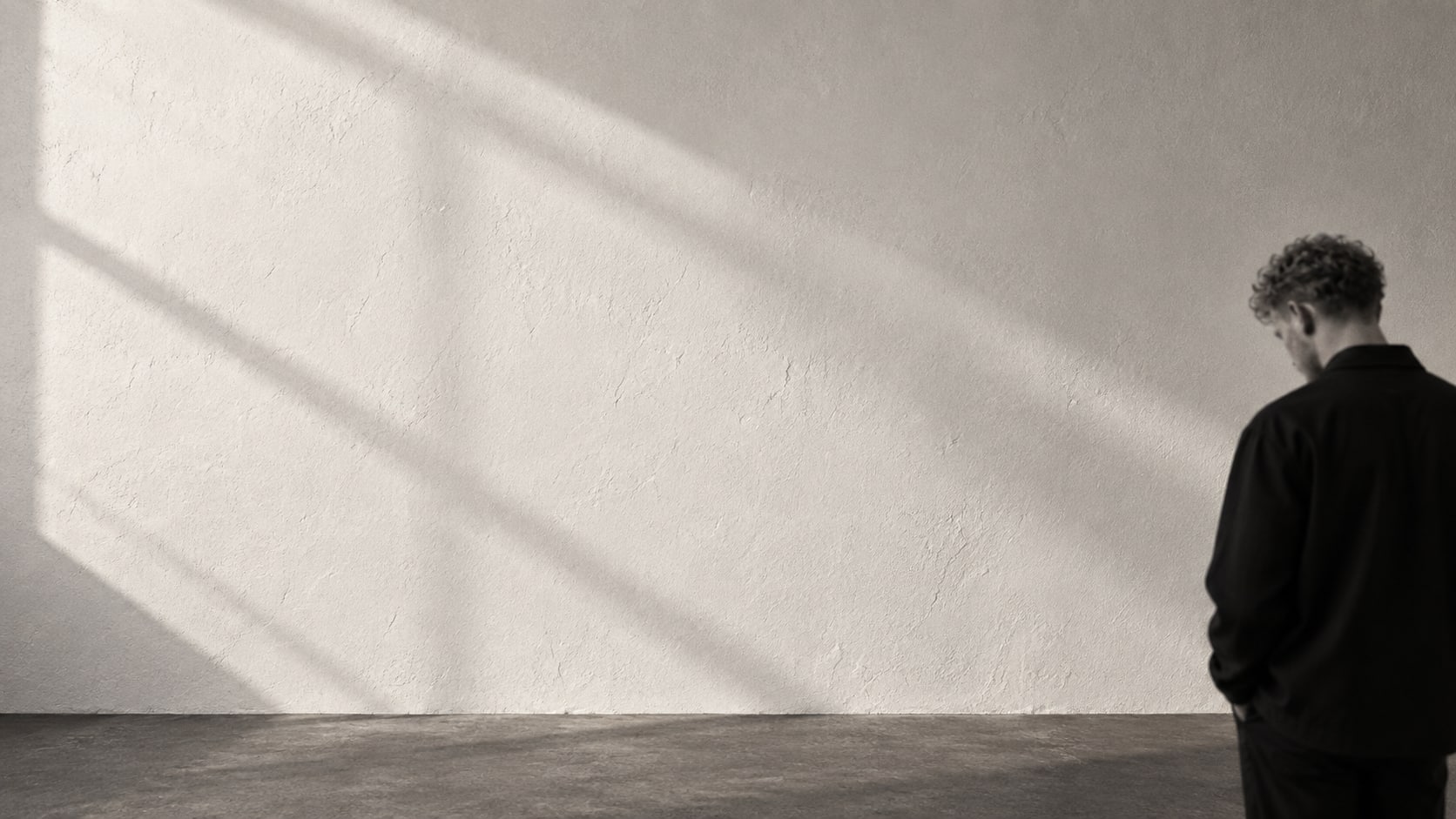 Soft light across a quiet studio wall, with Walid discreetly at the edge of the frame